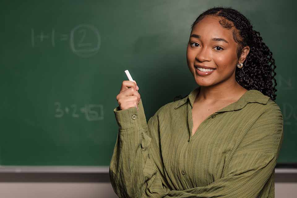 A headshot of Camille Fuller holding chalk in front of a blackboard