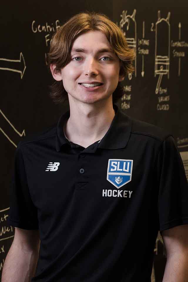 Keegan Hegger standing in a Billiken athletics shirt in front of a black board with equations