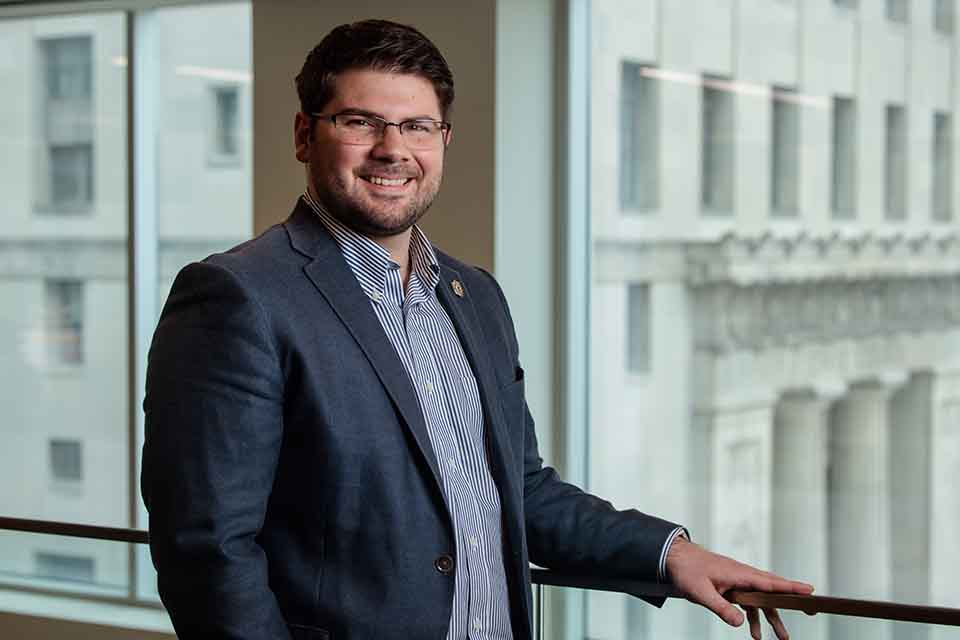 Nick Weaver standing in front of a glass balcony wall in front of a window at the law school