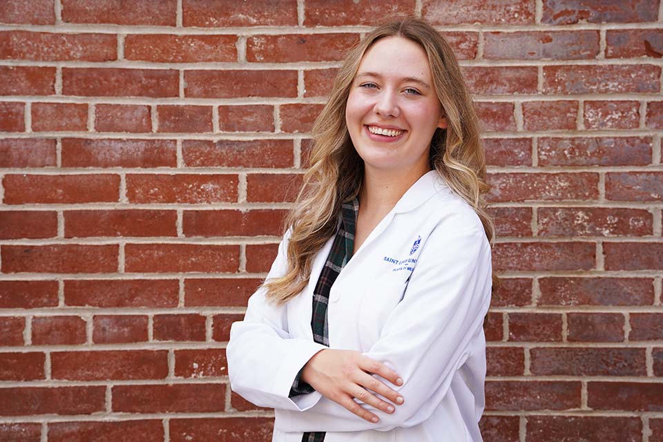 Caroline Kaczmarek wears a doctor's white coat and poses for a photo outside.