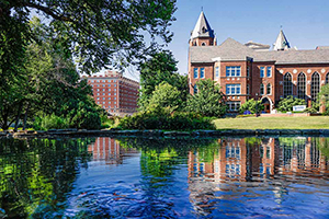 A brick building is reflected in a small pond on campus.