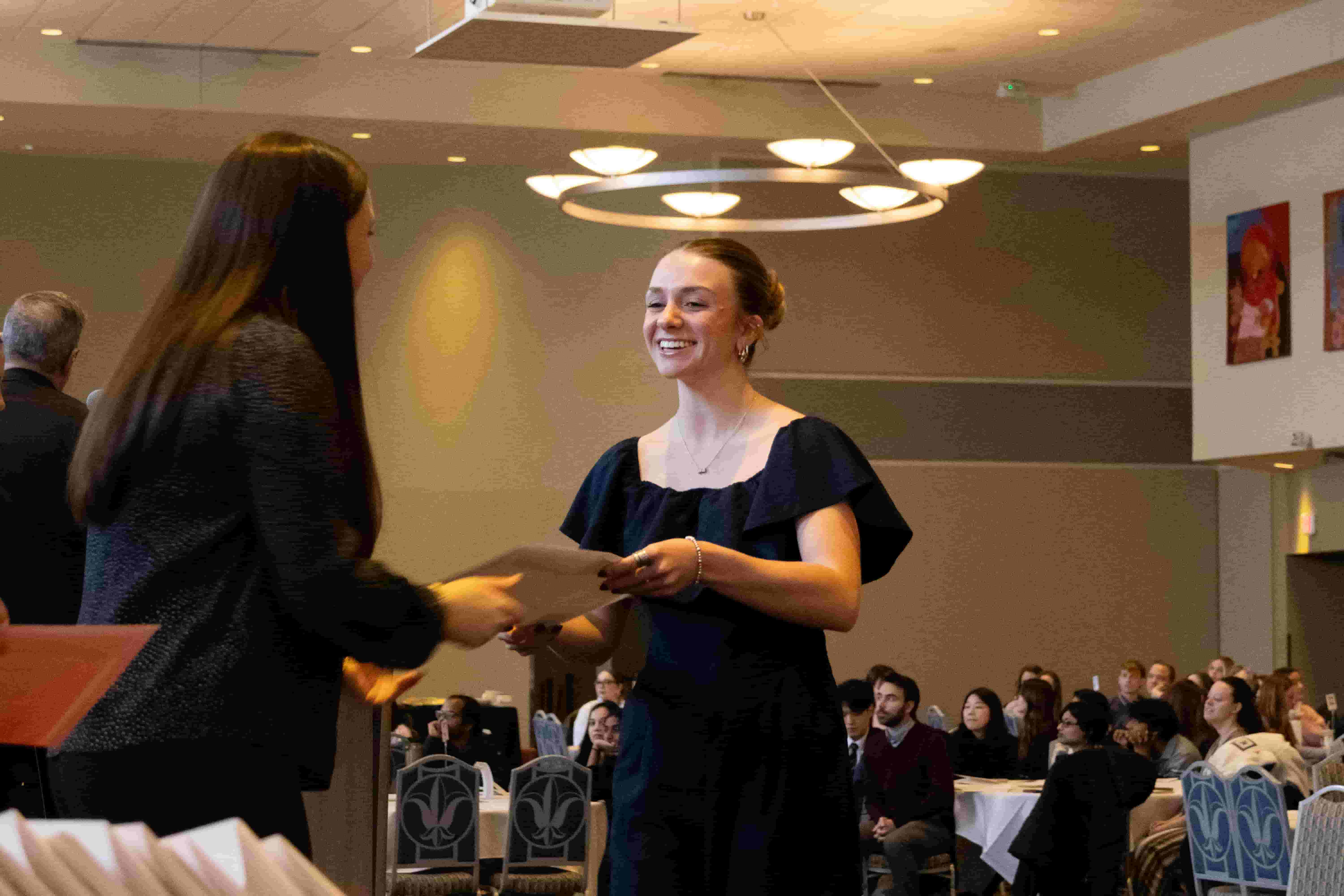 A student receives a certificate during a recognition ceremony as attendees look on.