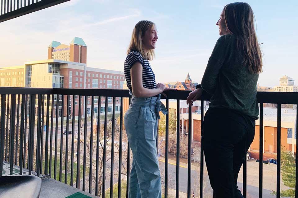Two female students standing on a balcony overlooking campus