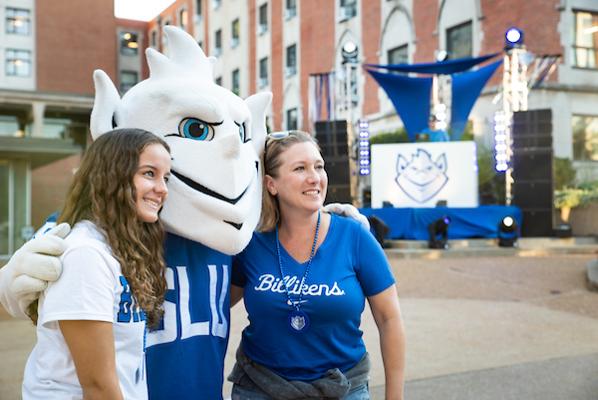A student and mother posing with the Billiken in front of a stage at 2021 Homecoming and Family Weekend