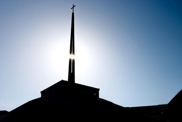 The cross atop the spire of SLU's Jesuit Center silhouetted against a blue sky