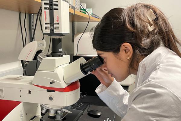 Kavya Haris looking into a microscope while wearing a lab coat