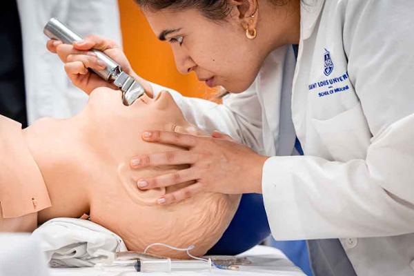 A student leans over a teaching manikin with a scope as she bends back its head