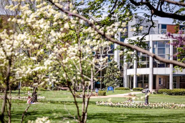 Exterior view of Pius Memorial Library in the background with flowering trees in the foreground. A statue of St. Ignatius is visible. 
