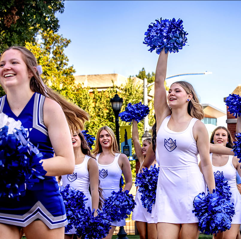 Cheerleaders holding pom poms walk on in a parade on the SLU campus.