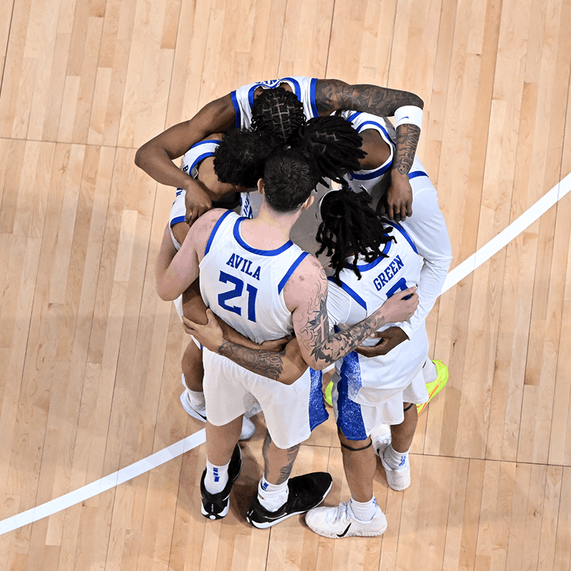 A group of basketball players forms a huddle on a basketball court.