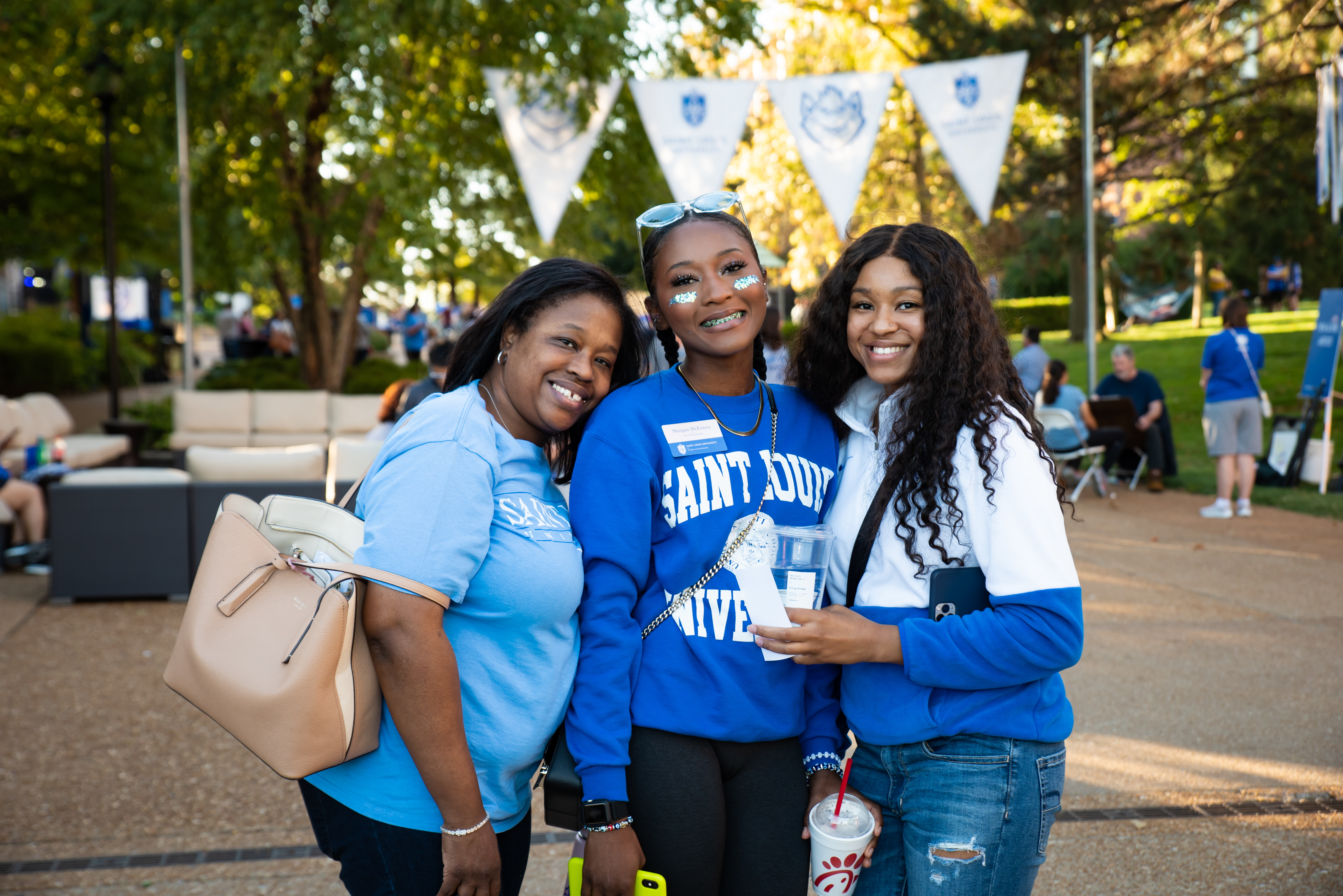 Three women wearing SLU shirts smile while standing under a homecoming banner.