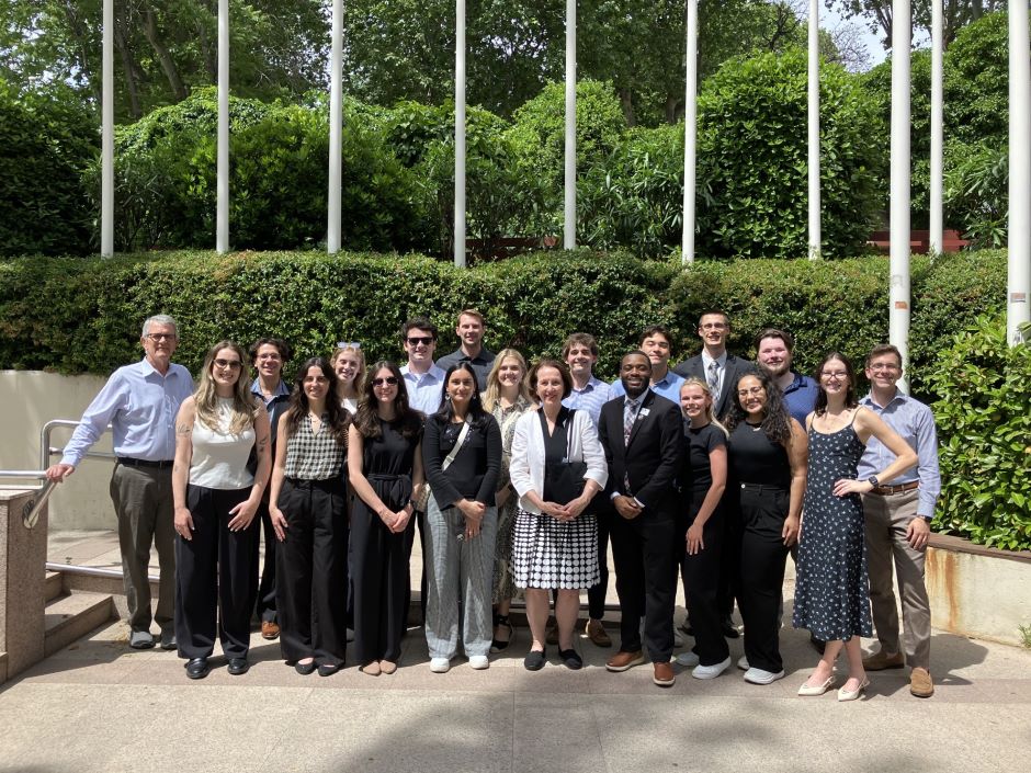 group of students and professors standing in front of a group of flags outside of the european commission group of students and professors stand outdoors in front of some bushes