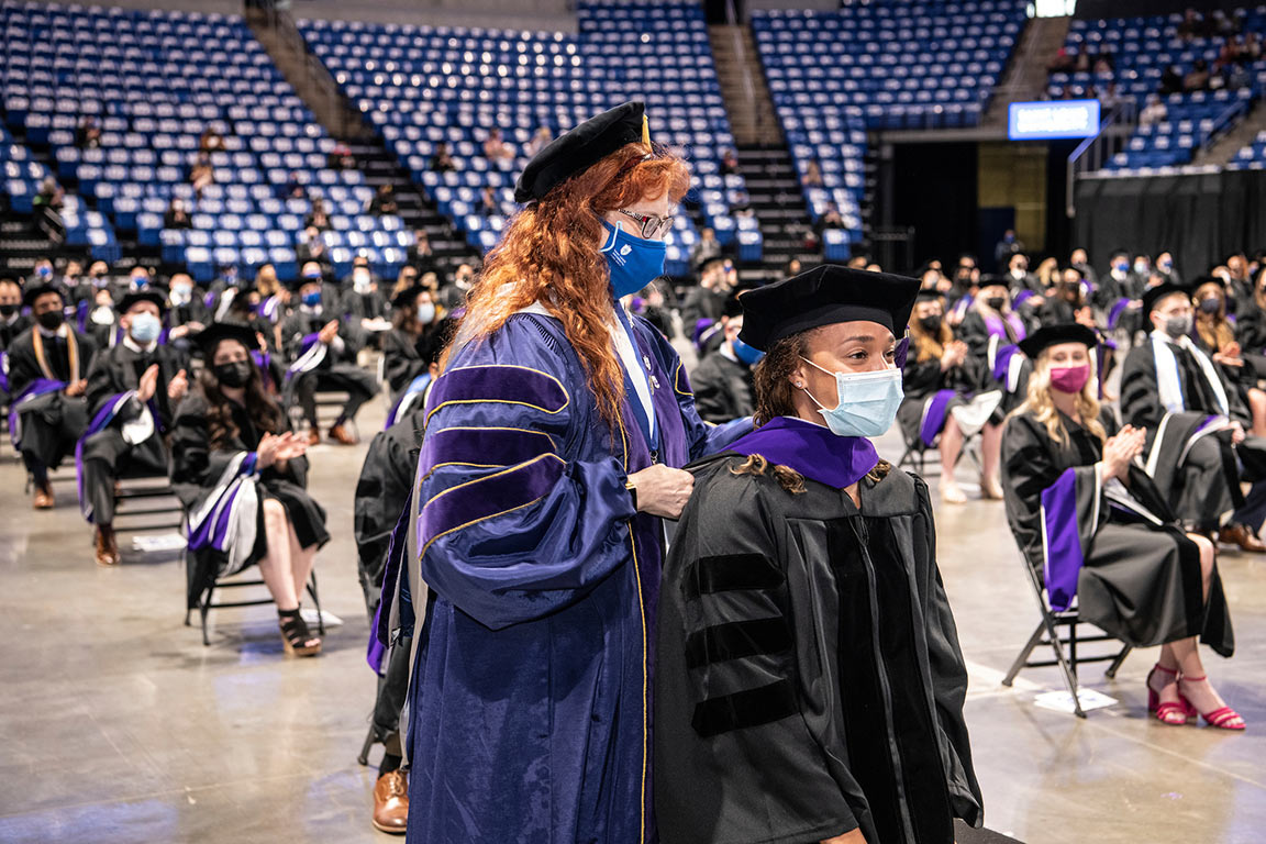 Prof. Yvette Joy Liebesman hoods graduates on the floor of Chaifetz Arena.