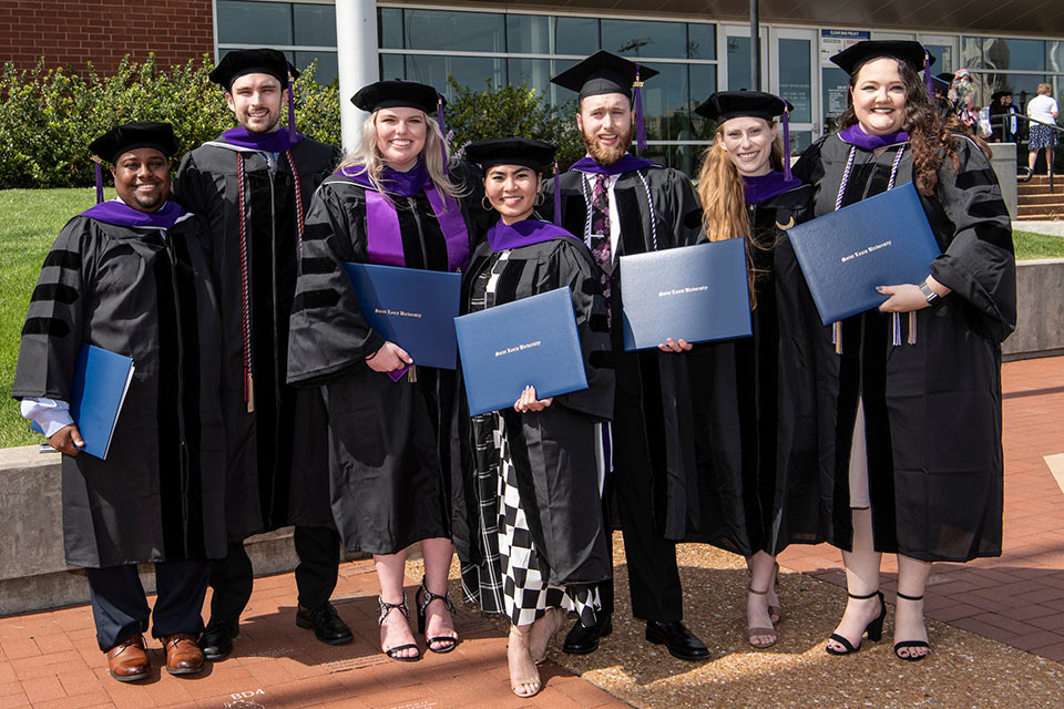 A group of law graduates pose outside Chaifetz Arena with their diplomas.