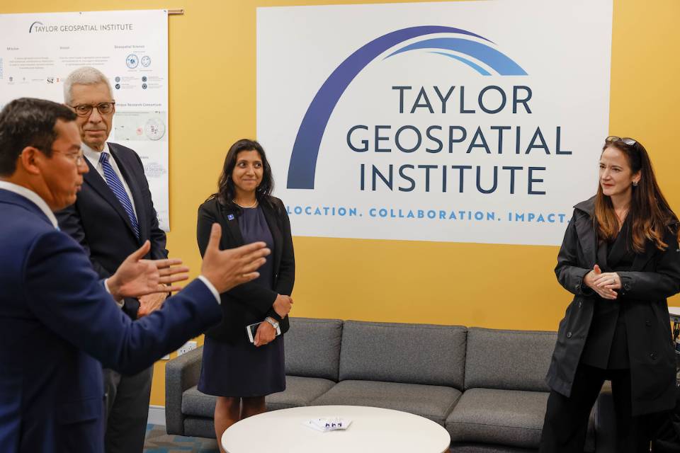 Four visitors to the Taylor Geospatial Institute have a discussion in front of the institute's sign.