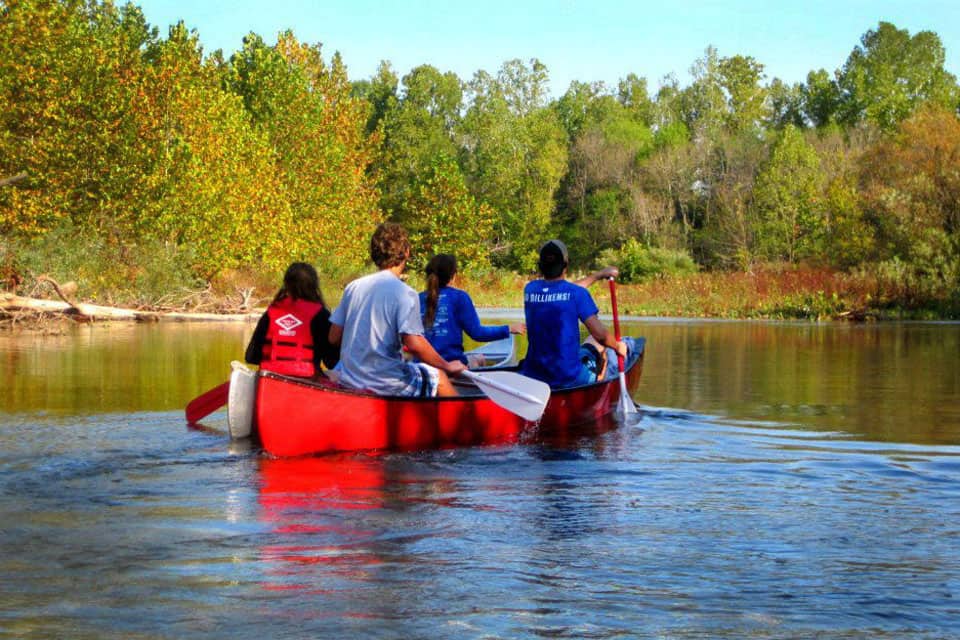 Four people seen from behind rowing a red canoe along a waterway