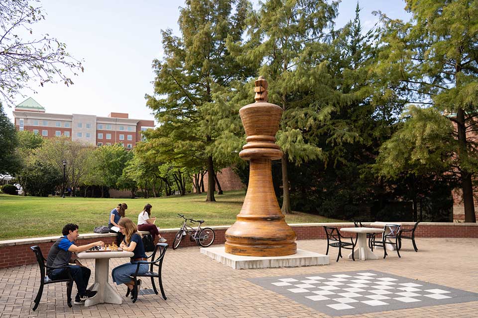 An exterior view of the chess commons featuring a large chess pawn and a sidewalk chess board.