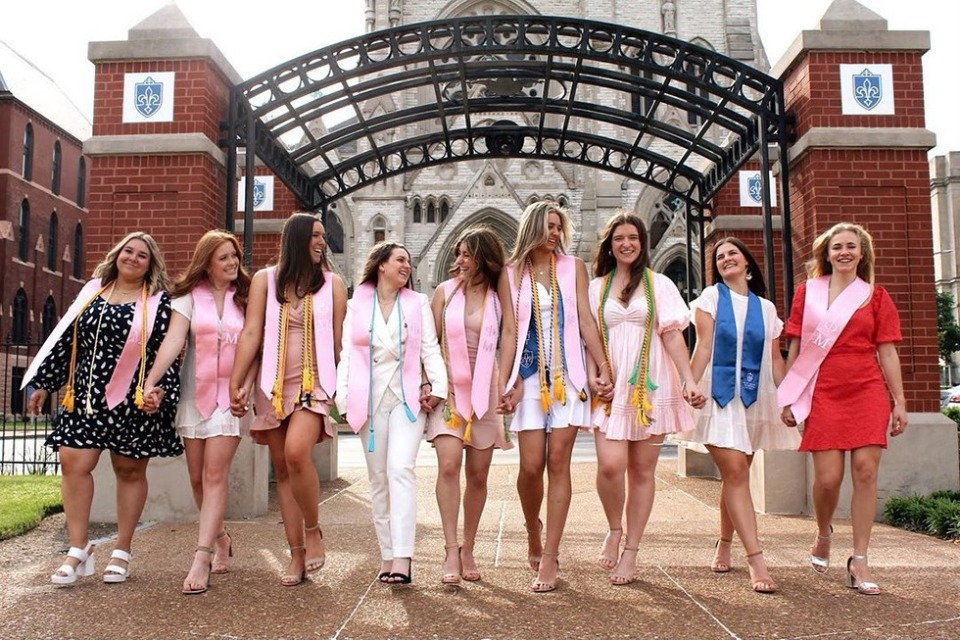 A group of sorority members wearing stolls walk in a row while holding hands on the SLU campus.