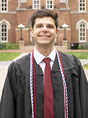 Man in a graduation gown in front of a brick academic building