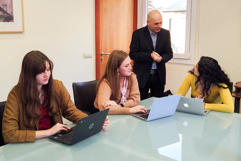 Three students with laptops talking with the professor