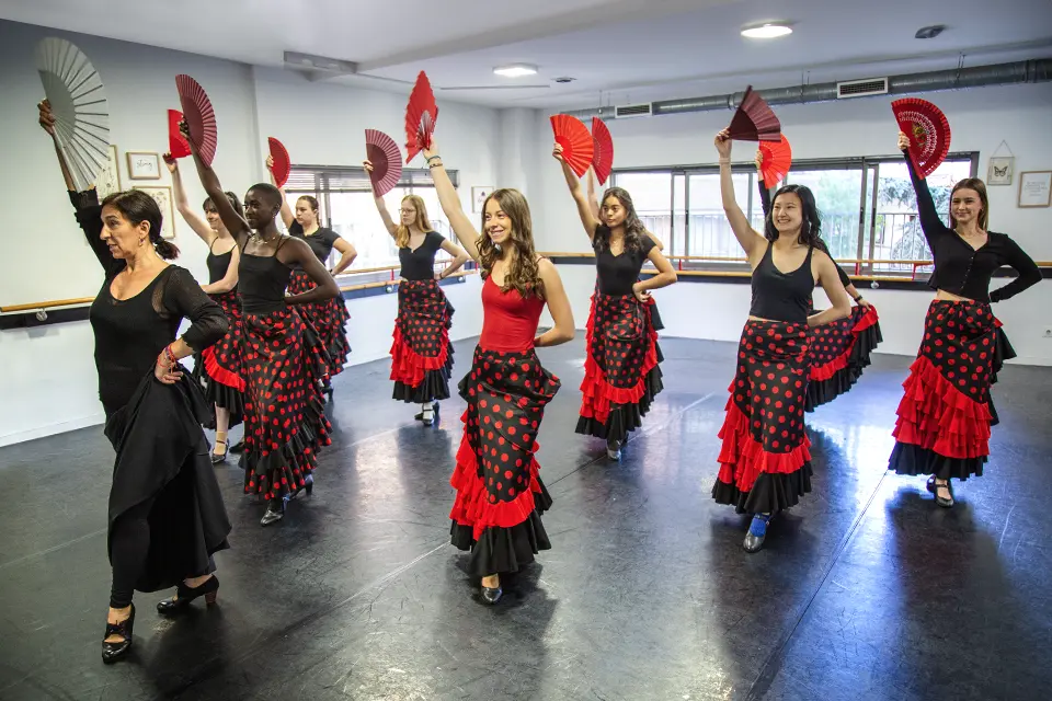 Student wearing long skirts and standing in rows dance with shawls during a flamenco class.