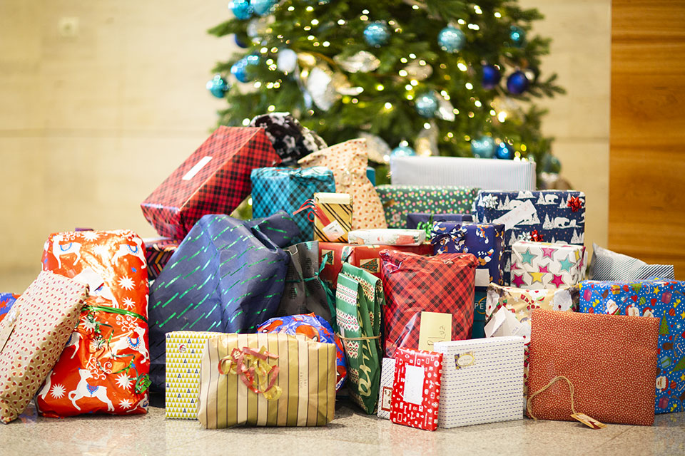 A variety of brightly wrapped Christmas gifts sit next to a Christmas tree.