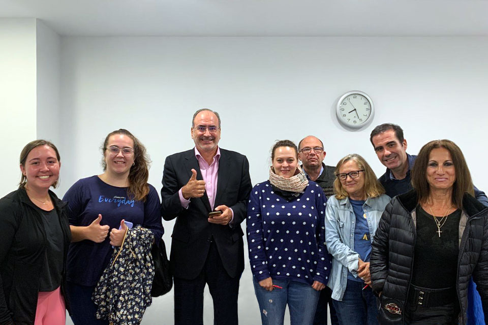 Participants in SLU-Madrid's English conversation classes stand and smile. Two give a thumbs up. Participants represent a range of ages and ethnicities.