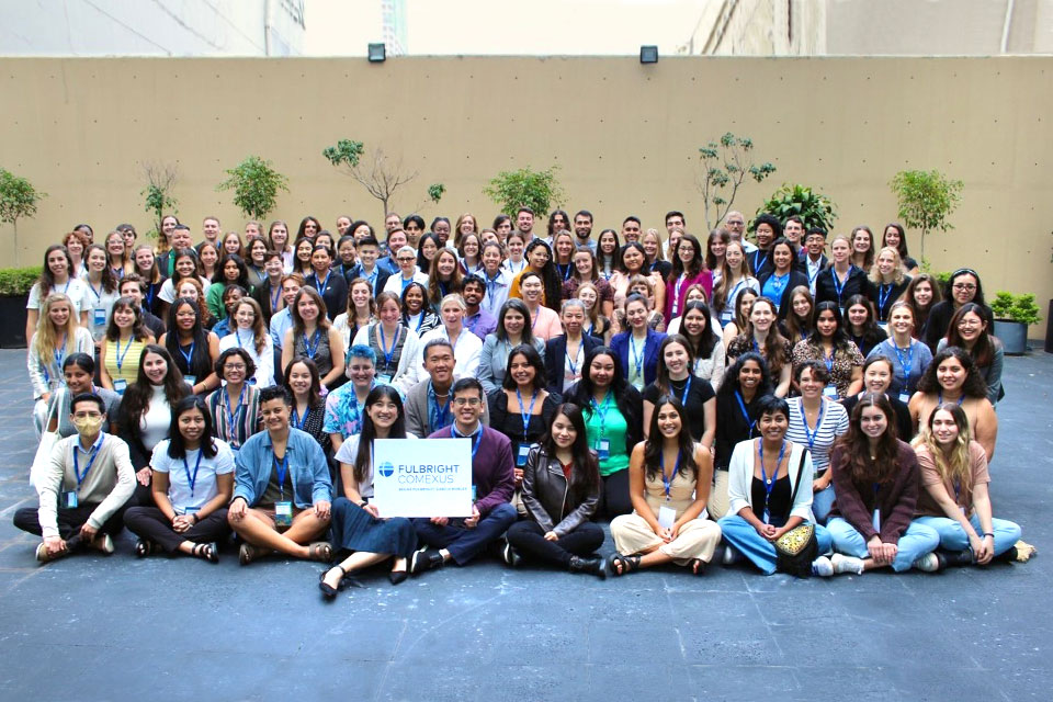 Several rows of students sitting and standing pose with a Fulbright sign.