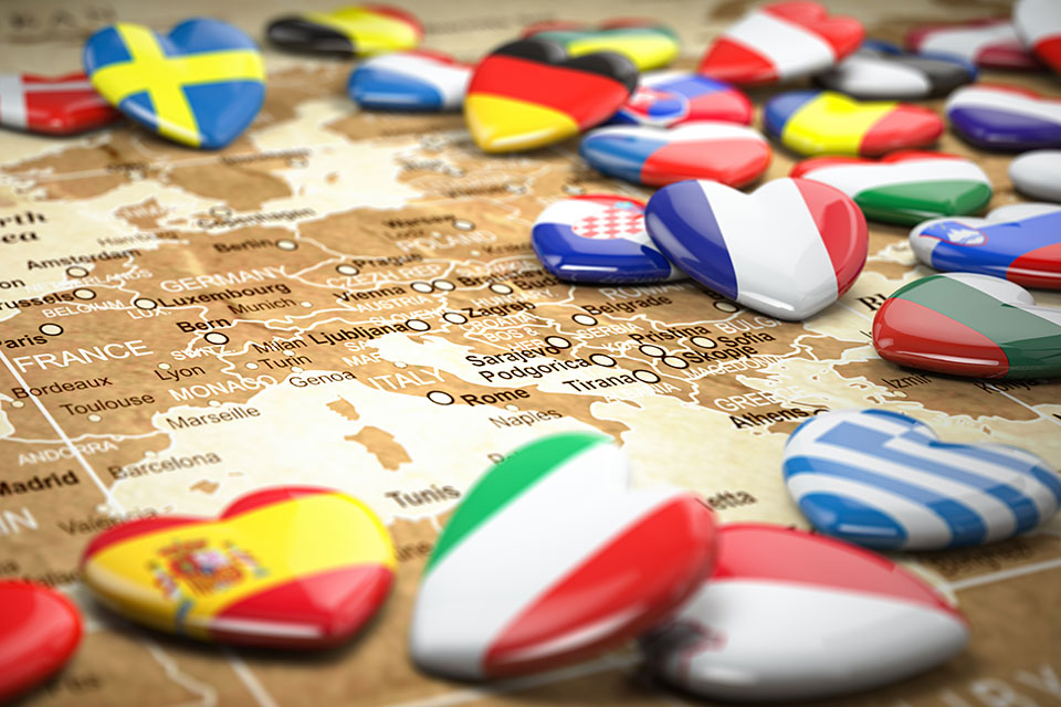 Photo illustration of a selection of heart-shaped pins with international flags is distributed across a map of Europe.