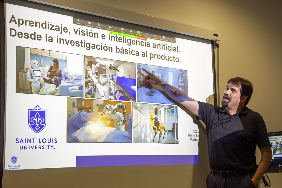 A presenter points at a large screen reading Aprendizaje, vision e inteligencia artificial. Desde la investigacion basica al producto. or Learning, vision and artificial intelligence. From basic research to product.