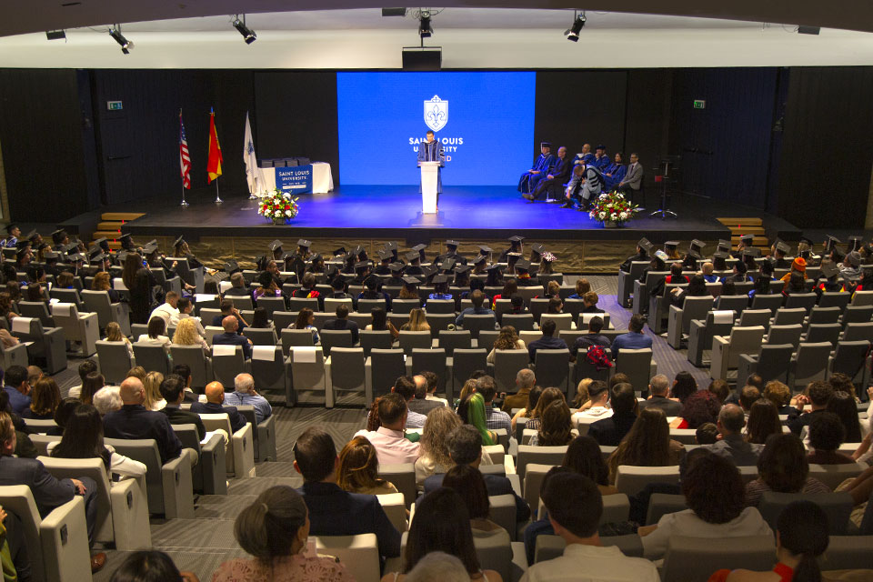 Graduates and audience members are shown from the back, watching a speaker on stage during the commencement ceremony of May 2023.