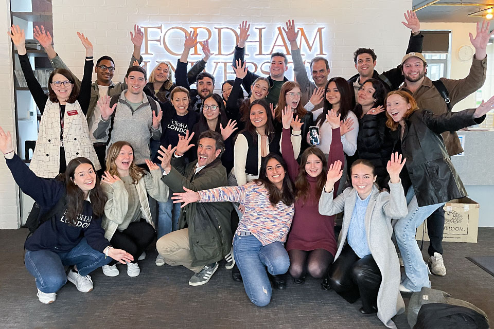 SLU-Madrid marketing students pose in front of a sign for Fordham University's London campus, waving their hands in the air.
