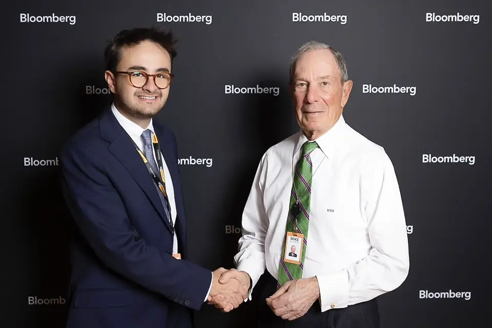 An alumni shaking hands with a man in front of a photocall.