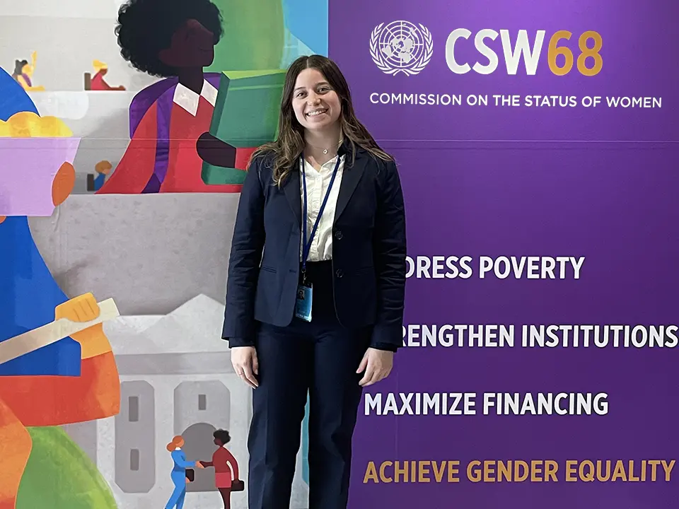 A student posing in front of of the Commission on the Status of Women poster in the background.