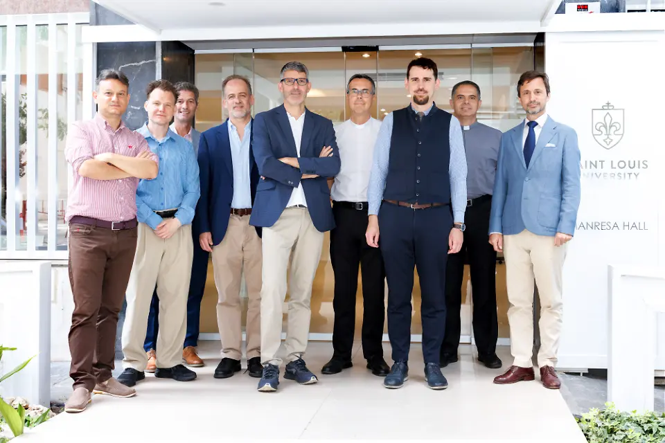 Nine individuals look at camera for group photo with building entrance in background.
