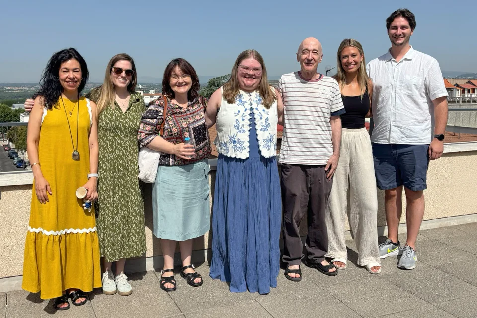 Seven Saint Louis University-Madrid M.A. in Spanish students and faculty members pose together on a campus rooftop terrace overlooking Madrid on a sunny day. The group smiles at the camera with the city skyline and blue sky in the background.