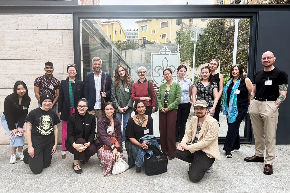 Conference participants pose for a group photo outside San Ignacio Hall with the University logo on the glass door behind them on glass.