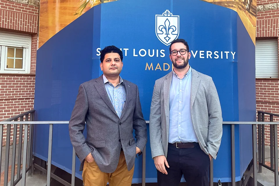 SLU-Madrid Expands Technology Training Through Cisco Networking Academy and PUE Academy Professor Rehman and PUE's Àngel Garcia pose outside the stairwell in Padre Arrupe Hall patio with the University logo behind them on the banner wrapping around the stairs.