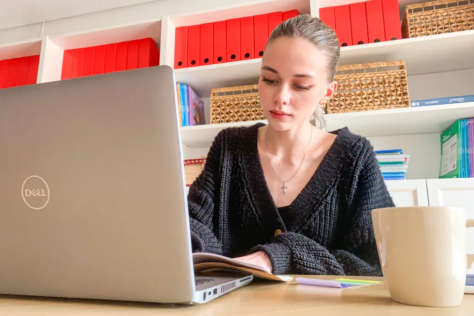 Student on her desktop with a laptop, reading a magazine with a cup on the table.. on the table.