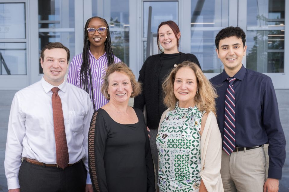 A group shot of smiling researchers standing outside an office building entrance.