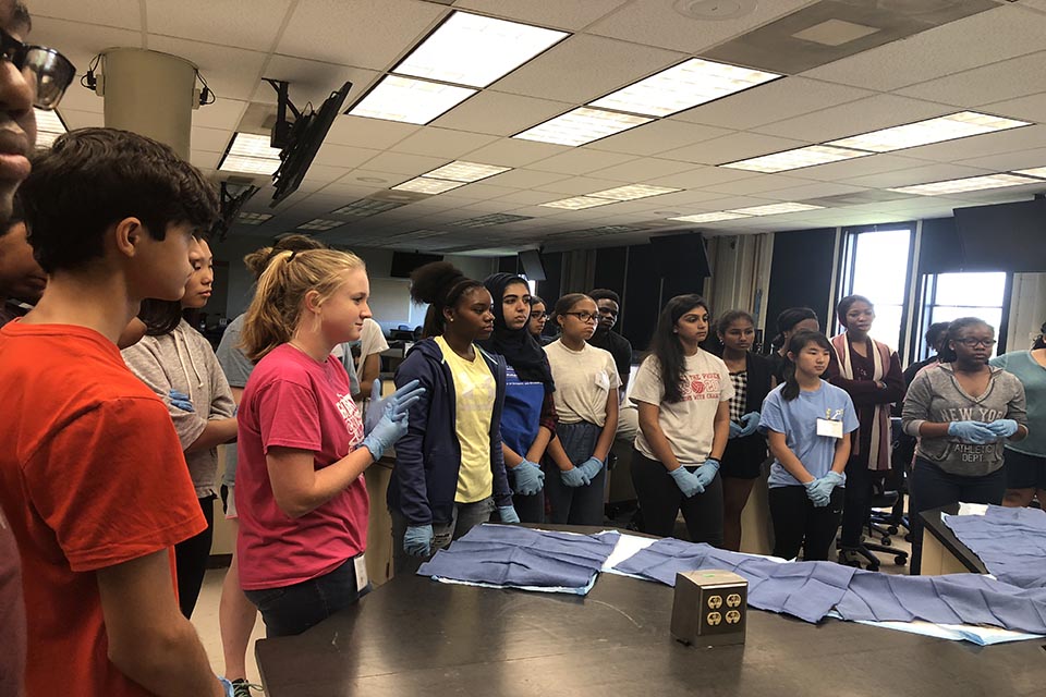 High school students wearing latex gloves stand around a lab table.