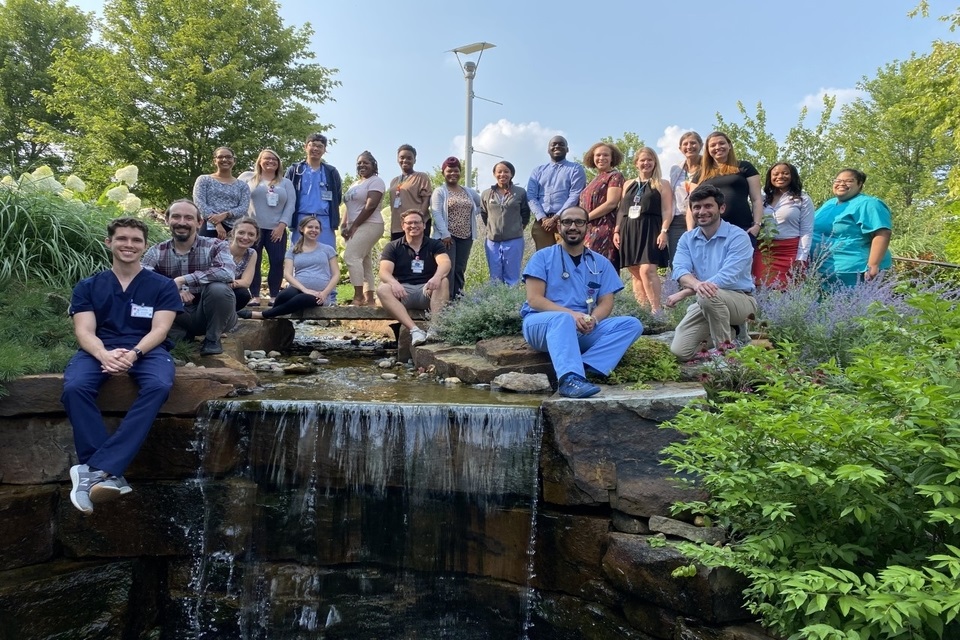 A group of more than 15 residents gather for a photo above a small waterfall on campus. They're smiling, and some are wearing scrubs.