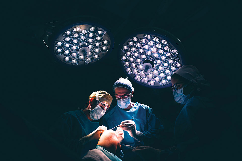 Medical students perform a procedure on a patient's knee under bright lights.