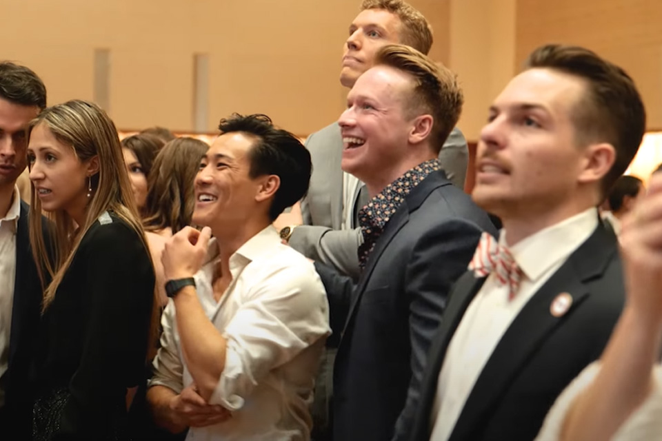 Students standing in a row and looking up at something.. Most are smiling.