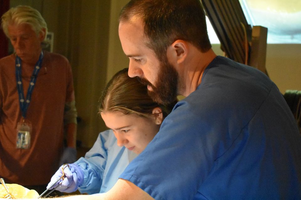 An instructor stands next to a student handling surgical forceps.