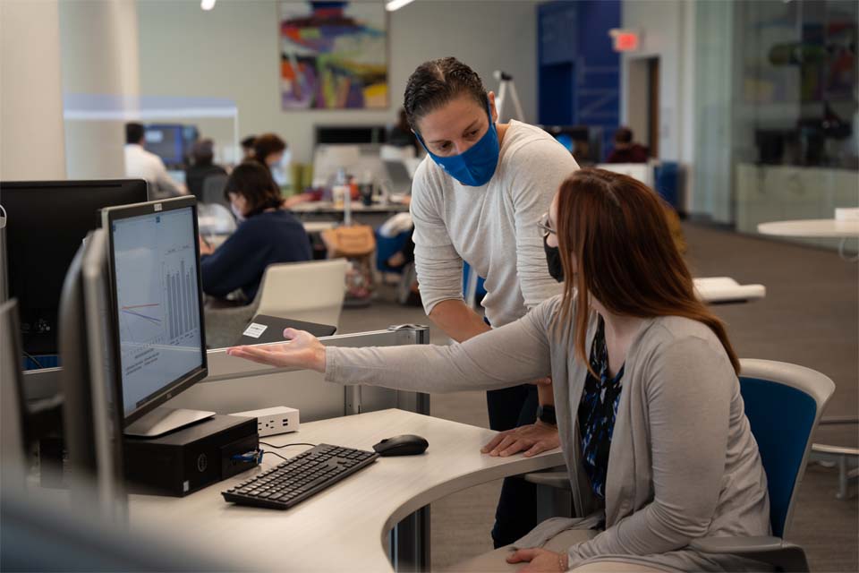 An instructor talks to a student who is working on a computer.
