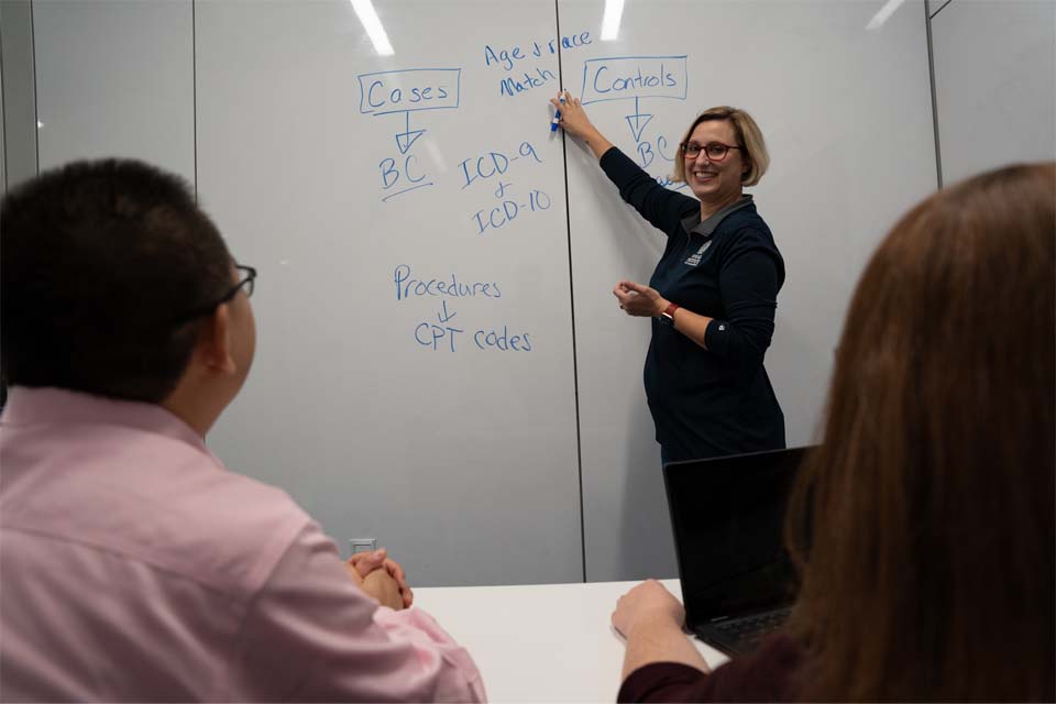 Instructor smiling in front of a white board with two students facing them