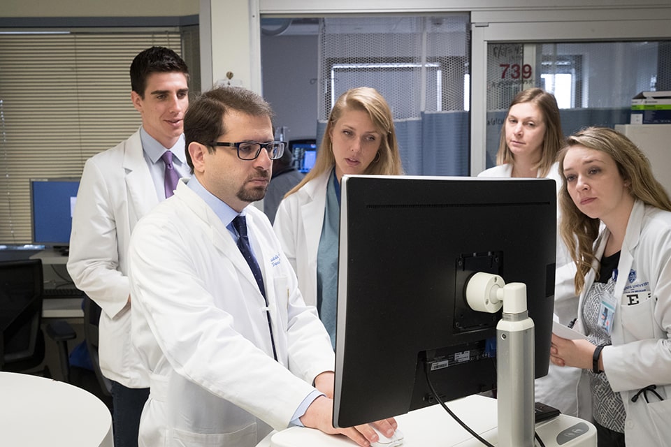 Four clerkship participants observe as a faculty member types on a computer.