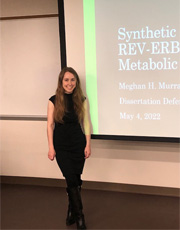Picture of Meghan Murrany standing infron of a screen projection with her dissertain defense presentation