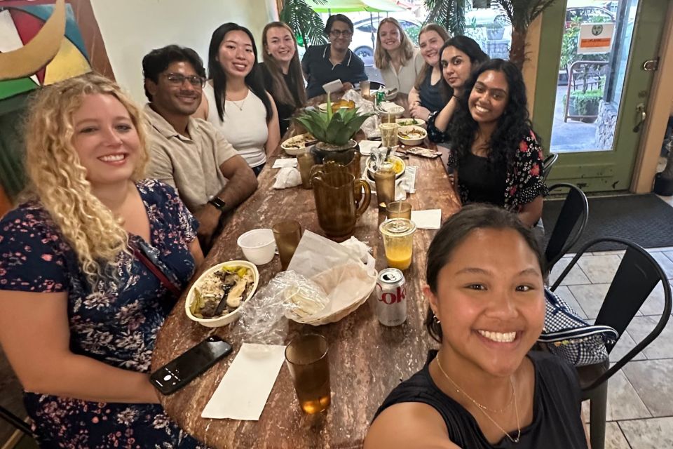 A group of smiling students sitting along a long dinner table inside a restaurant.